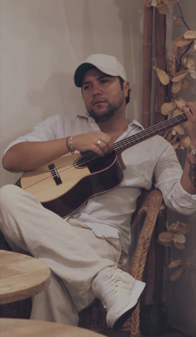 Leon Gabriel with a guitar in a wicker armchair